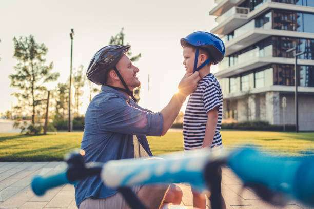 Father helping cheerful son wearing bike helmet