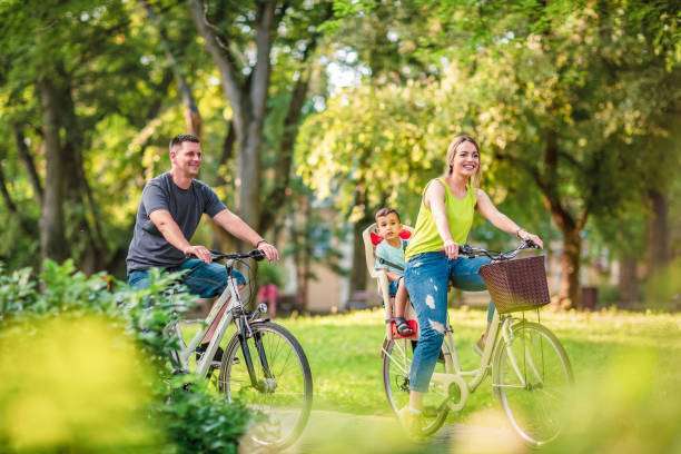Happy active father and mother with kid on bicycles having fun in park bike helmet