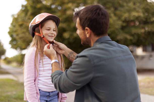 Happy Father Helping Cute Daughter With Bike Helmet While Cycling in in the City Suburbs