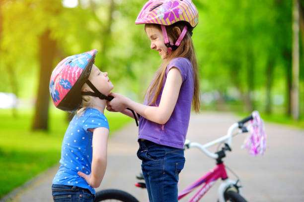 Adorable girl helping her little sister to put a bike helmet on