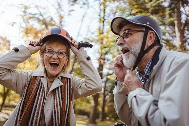 Joyful senior couple putting on bike helmets in a park