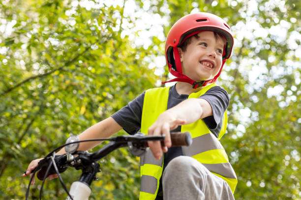 Happy boy in red bike helmet and safety vest rides bike.