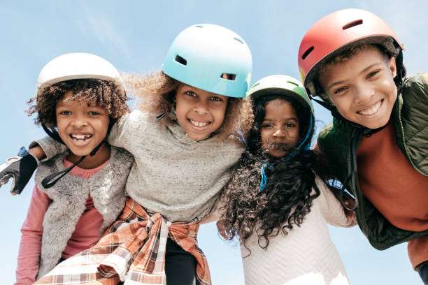 Four smiling children wearing colorful bike helmets outdoors.