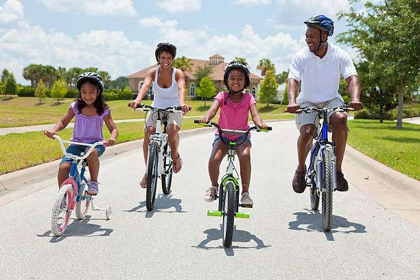 Family cycling on a sunny day, all wearing bike helmets.