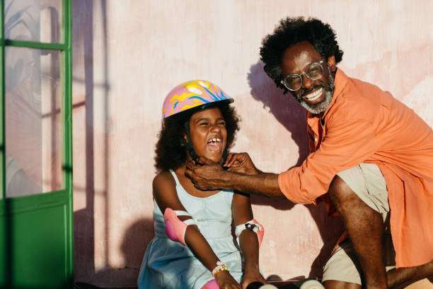 Man helps happy girl with a colorful bike helmet adjust her roller skates outdoors.