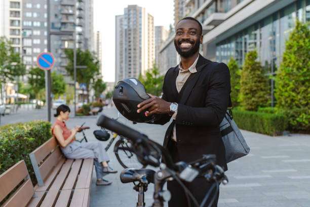 Smiling businessman holds his black bike helmet next to his bicycle in a city.
