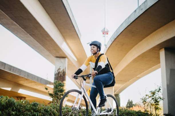 Young woman in black bike helmet rides bicycle under overpass.