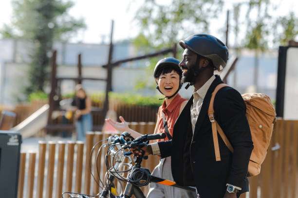 Smiling diverse couple wearing bike helmets, standing with their bicycles in a park.