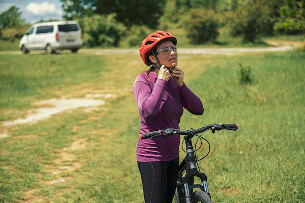 Woman in orange bike helmet secures straps before cycling.