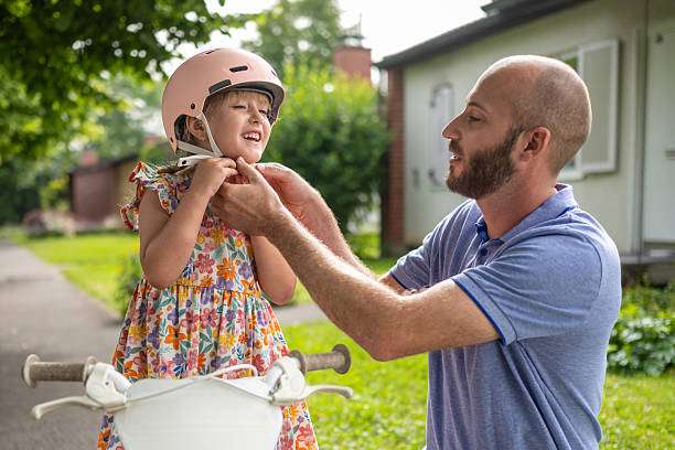 Father secures child's pink bike helmet.