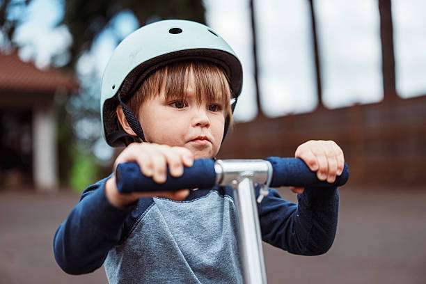 boy wearing a bike helmet rides a scooter in the driveway