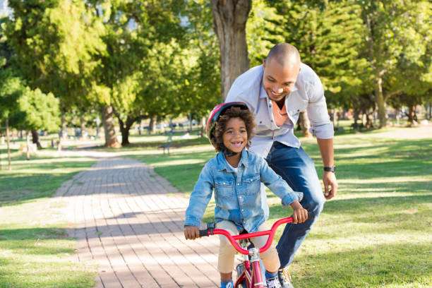 Father teaches son to ride bike, son wears bike helmet.